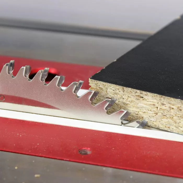 Close-up of a circular saw blade cutting a black laminated particle board on a table saw.