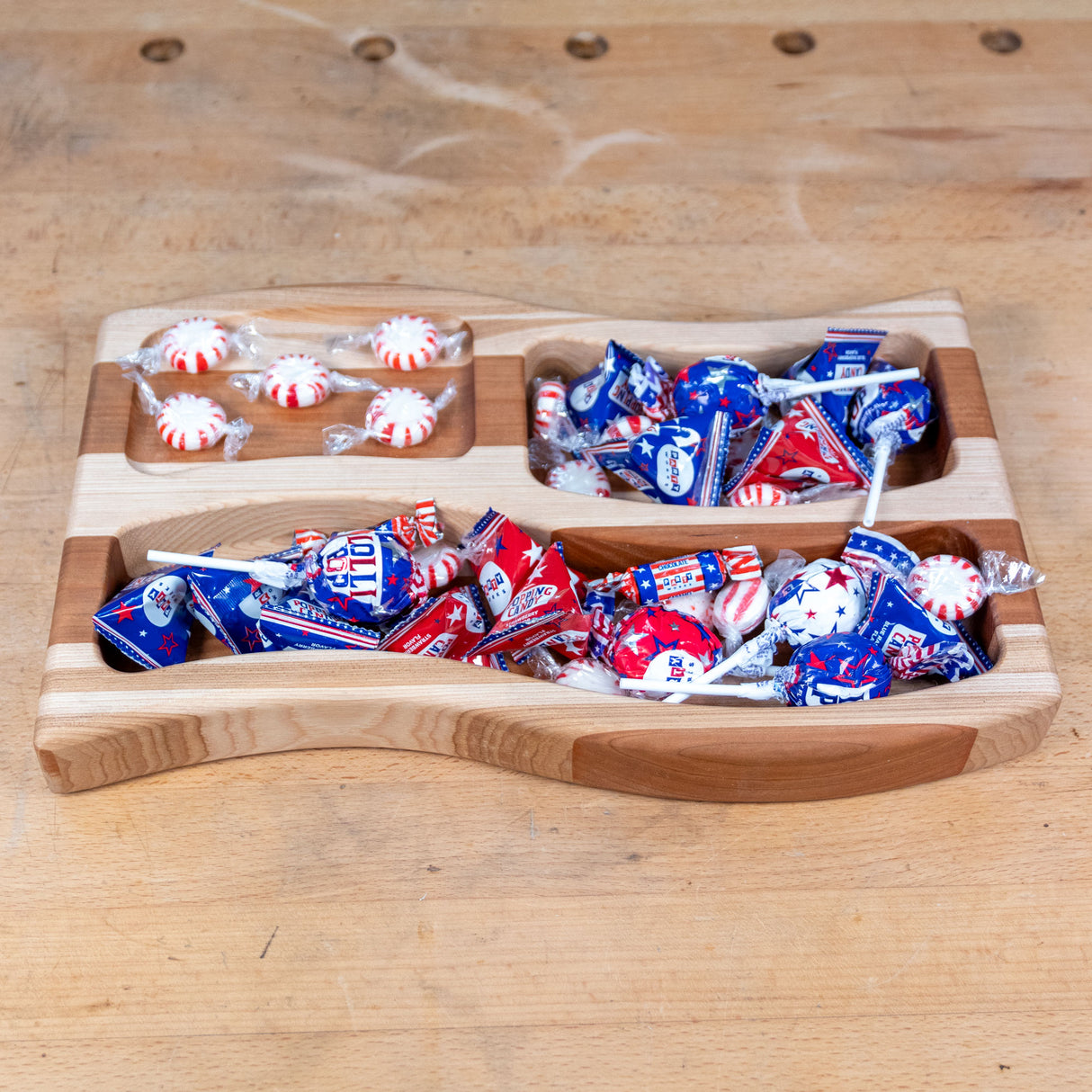 Wooden flag-shaped candy tray filled with red, white, and blue sweets on a workbench