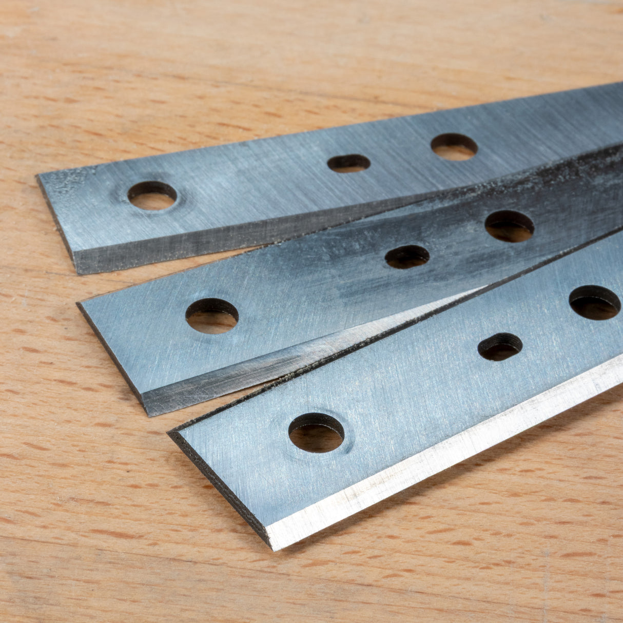 Closeup of replacement planer knives with mounting holes on a wooden surface