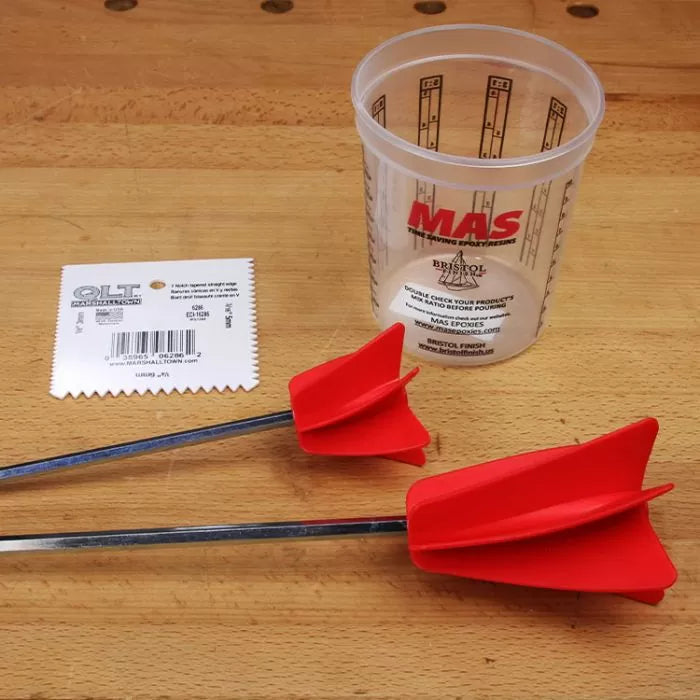 Woodworking epoxy mixing cup, red mixer paddles, and notched spreader on a workbench