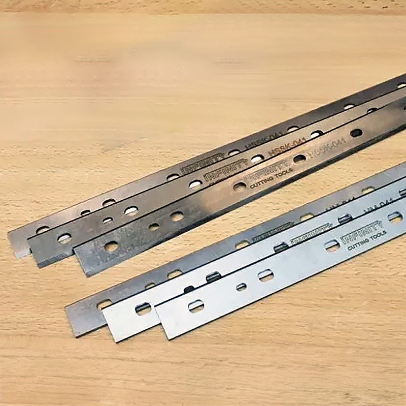 Steel planer blades with holes for woodworking, displayed on a wooden surface