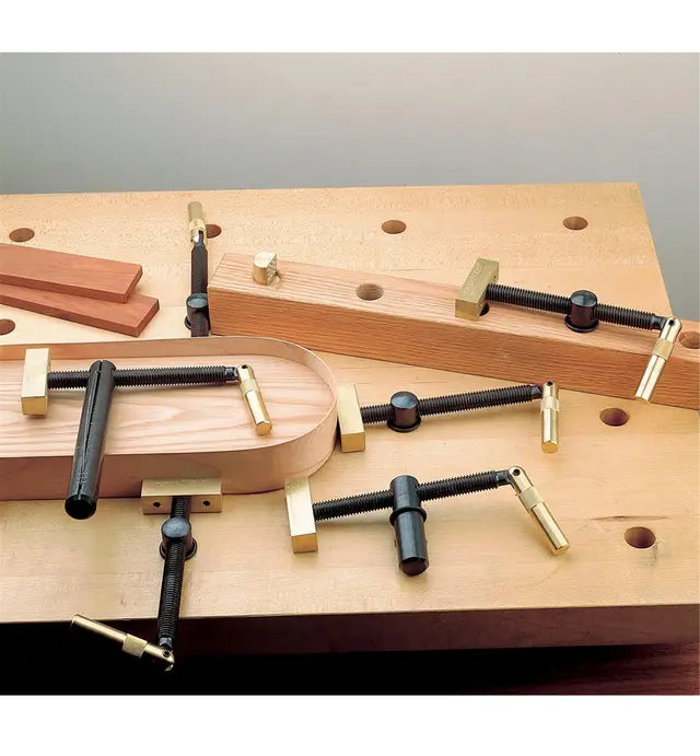 Woodworking holdfast clamps securing wood pieces on a workbench with dog holes.