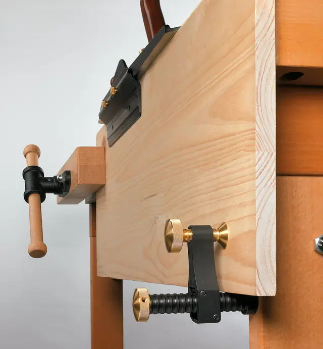 Woodworking vise with brass hardware mounted on workbench, hand saw resting on bench