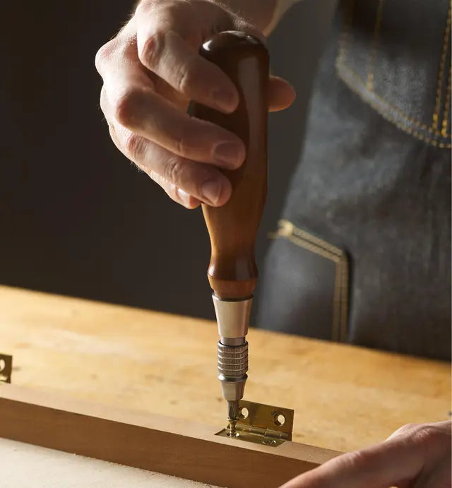 Hand using a woodworking screwdriver to install brass hinge on wood project