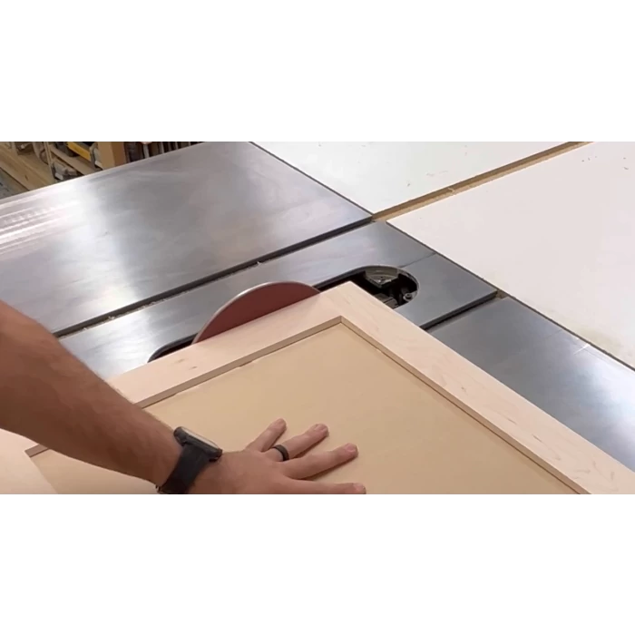 Woodworker cutting panel on table saw with safety hand placement in workshop