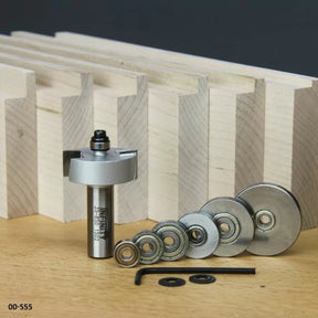 Router bit set with bearings and tools for woodworking joinery, displayed on workbench with dovetail boards.