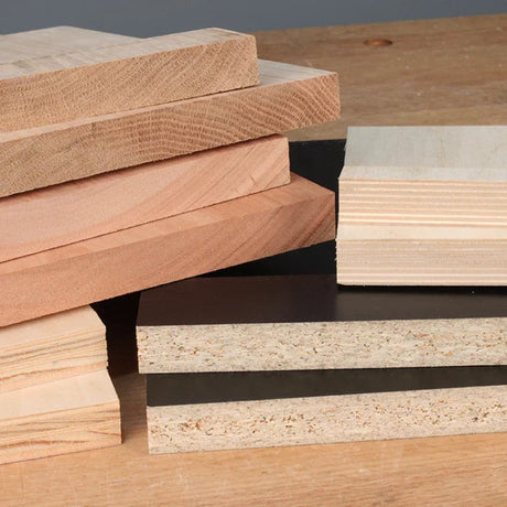 Stack of assorted hardwood and engineered wood boards on a workbench for woodworking projects