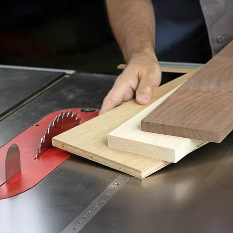 Hand holding wood boards next to table saw blade in woodworking shop