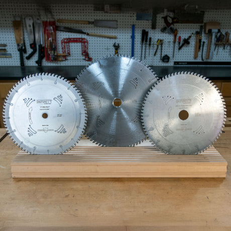 Three circular miter saw blades displayed upright on a wooden workbench in a workshop