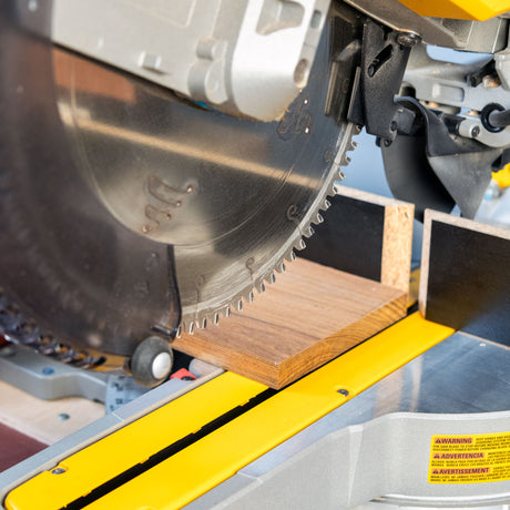 Close-up of miter saw blade cutting wood on a yellow miter saw workstation