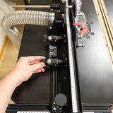 Hand adjusting micro dial on precision router table fence with dust collection hose attached
