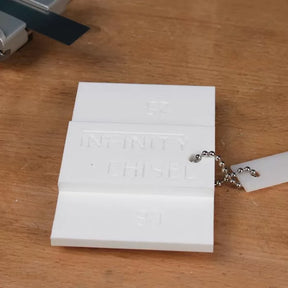 White plastic chisel gauge with chain for woodworking tools on a wooden surface.