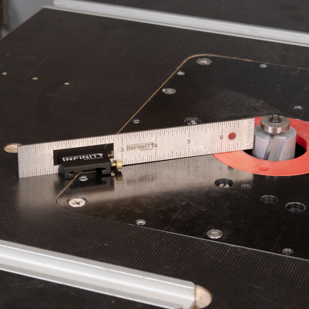 Close-up of a router table with a metal ruler and infinity branding on a black surface.