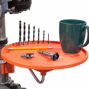 Round orange drill press tray holding drill bits, a pencil, two forstner bits, and a coffee mug