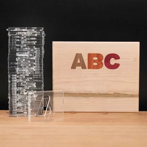 Acrylic router templates stacked beside a wooden box with multicolored ABC inlays for woodworking.