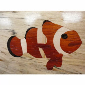 Wood inlay of clownfish with orange, white, and black details on a light wood background