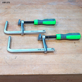 Pair of metal woodworking clamps with green handles on a workbench