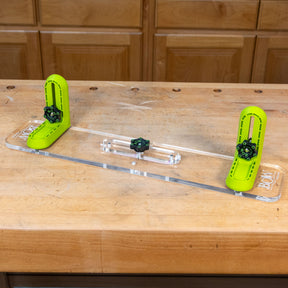Adjustable L-fence woodworking jig with clear acrylic base and green brackets on workbench