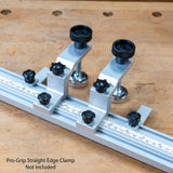 A close-up of a silver metal straight edge clamp with black adjustment knobs and measurement markings, placed on a wooden workbench. Text at the bottom reads 'Pro-Grip Straight Edge Clamp Not Included'.