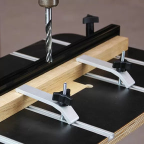 Drill press table with aluminum hold-down clamps securing wood for precise drilling