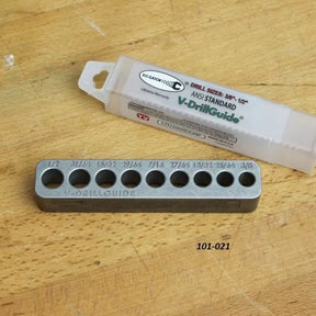 Metal V-DrillGuide drill guide tool with labeled hole sizes on wood surface, packaging included