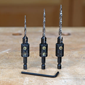 Set of three woodworking drill bits with countersinks and hex key on a workbench
