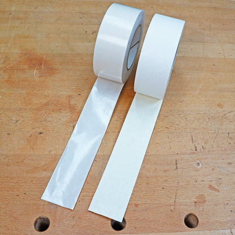 Two rolls of double-sided woodworking tape unspooled on a wood workbench.