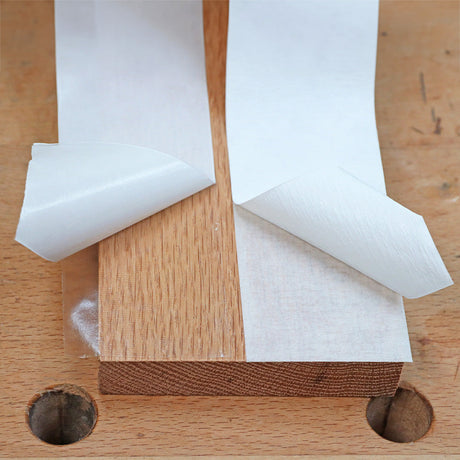 Double-sided woodworking tape on wood block, backing partially peeled for adhesive use