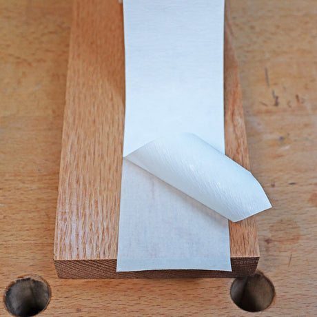 Double-sided woodworking tape being peeled from a wooden board on a workbench