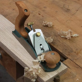 Bench hand plane shaping wood with shavings on a woodworking workbench