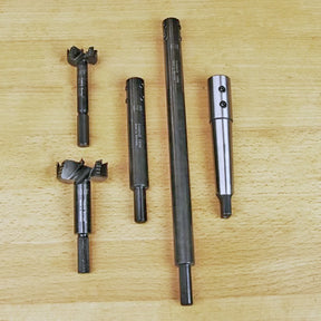 Five woodworking boring bits and extensions on a wood surface, precision cutting tools