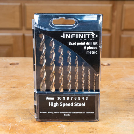 Metric brad point drill bit set, 8 pieces, high speed steel in packaging on wooden workbench.