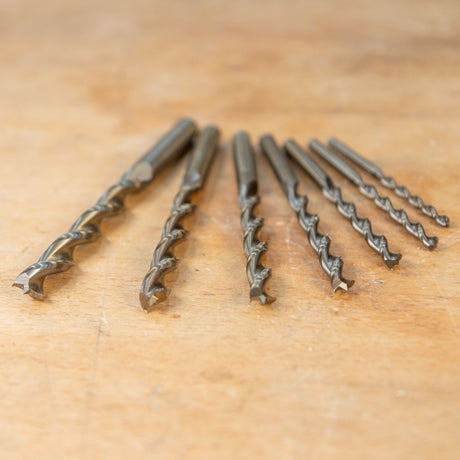 Set of seven woodworking drill bits with sharp tips on a wooden workbench