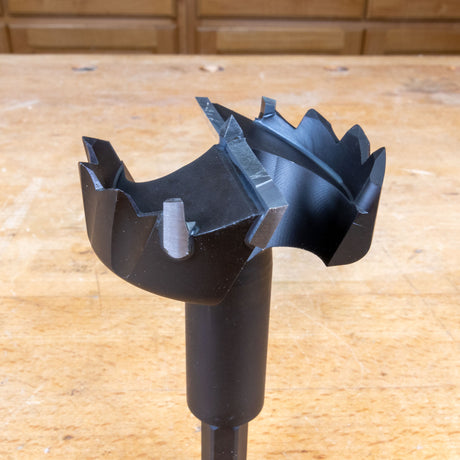 Close-up of a large carbide-tipped woodworking drill bit on a workshop bench