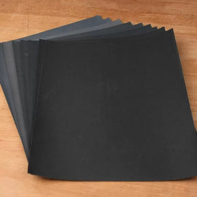 Assorted black and gray sandpaper sheets for woodworking on a wooden surface