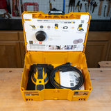 Mirka electric random orbital sander in a yellow case on a wooden table with a workshop background.