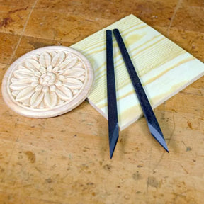 Wood carving tools with v-shaped tips, wooden carving sample, and wood block on workbench