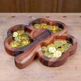 Shamrock-shaped wooden tray holding gold foil chocolate coins on a workbench.