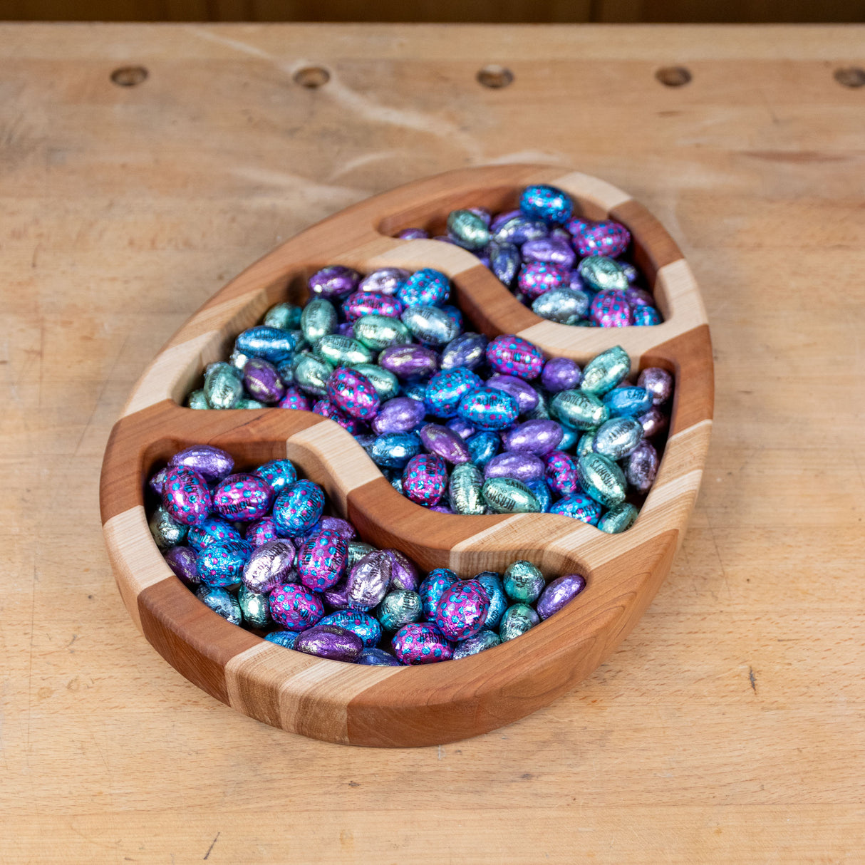 Wooden egg-shaped tray filled with colorful foil-wrapped Easter candies on a workbench