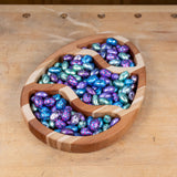 Wooden egg-shaped tray filled with colorful foil-wrapped Easter candies on a workbench