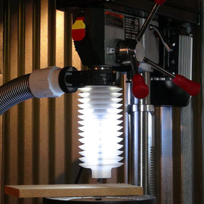 Drill press with dust collection hose and clear safety guard above a wooden board