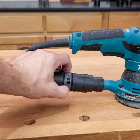Hand attaching dust hose to orbital sander on woodworking bench, workshop background