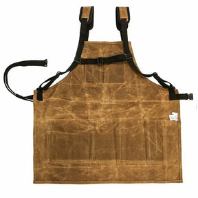 Brown waxed canvas woodworking apron with adjustable straps and front pockets, laid flat.