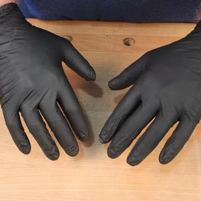 Black nitrile disposable gloves worn on hands, shown over a woodworking bench.