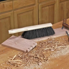 Woodworking bench brush with black bristles cleaning wood shavings on a workbench