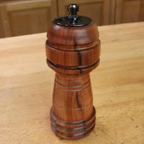 Handcrafted wooden pepper mill with dark grain on a woodworking bench