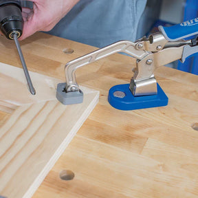 Woodworking bench clamp securing a wooden board while a drill drives a screw