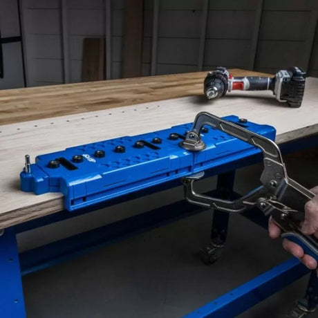 Blue pocket hole jig clamped to workbench for woodworking, cordless drill nearby