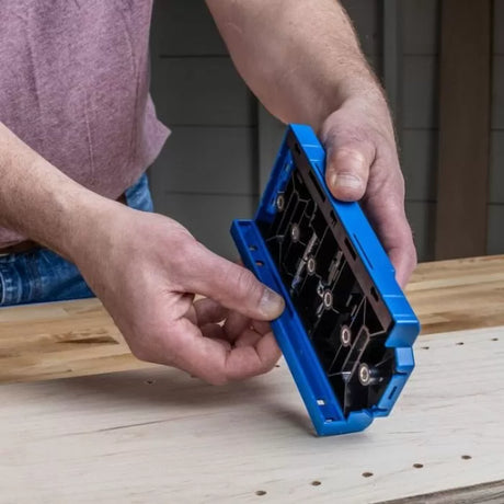 Woodworker using blue dowel jig on unfinished wood panel for accurate hole drilling