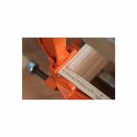 Woodworking corner joint clamped with an orange bar clamp on a workbench